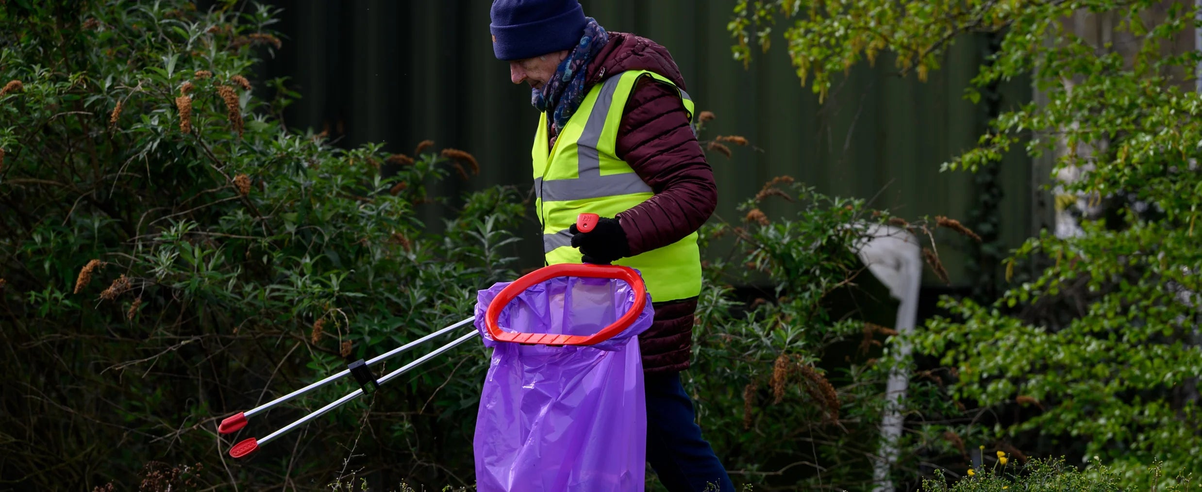 A volunteer picking up litter with a high vis and a hoop