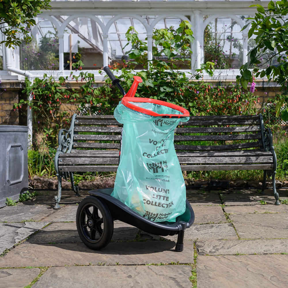 Green plastic bag with red handles on a wheeled cart in a garden setting