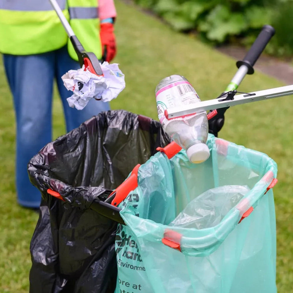 Person cleaning up trash with a litter picker on a grassy area