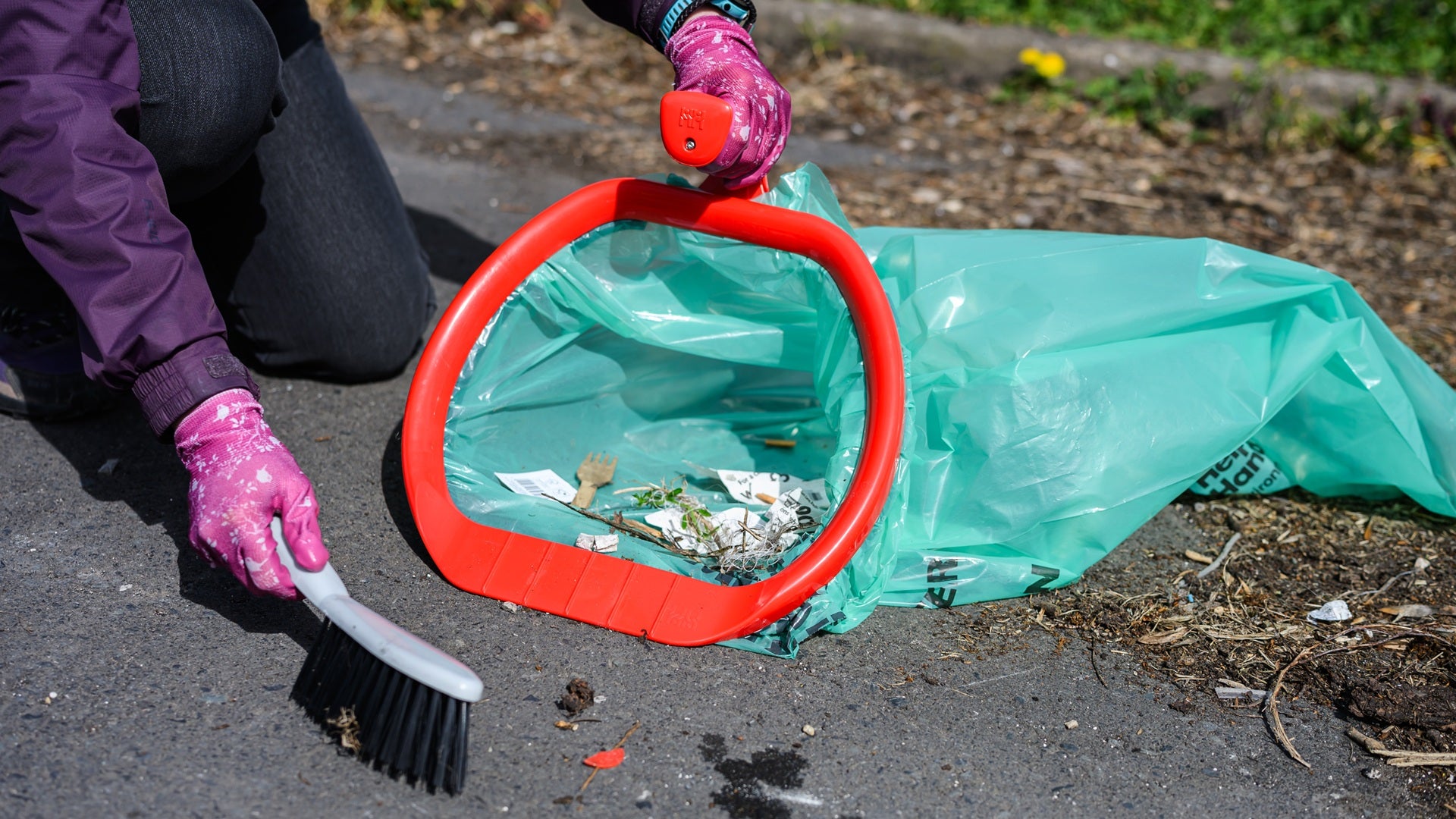 Someone sweeping rubbish into a bin bag using a hoop
