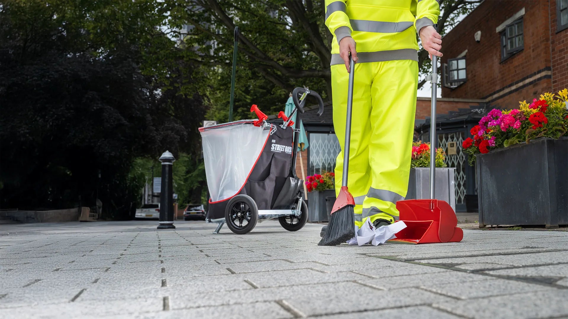 Person in high-visibility clothing with the Street Boss litter cart and cleaning equipment on a paved area.