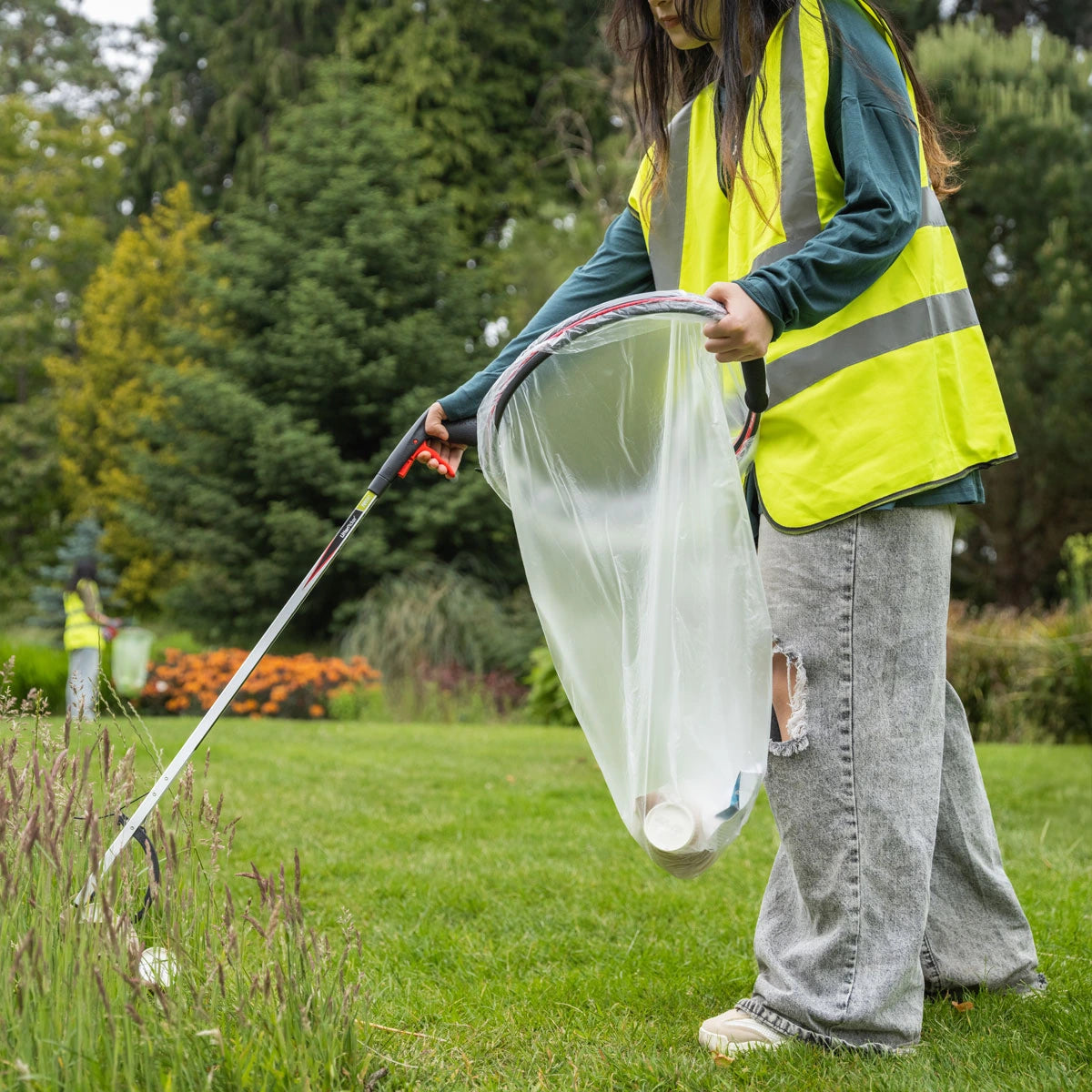 Person in a yellow safety vest cleaning up trash in a park with Helping Hand grabber.