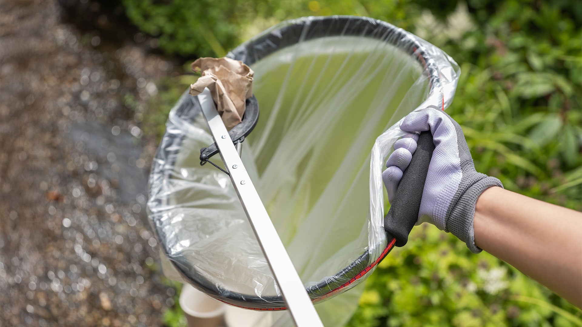 Person using a Handy Hoop and trash picker to collect paper rubbish greenery in the background.