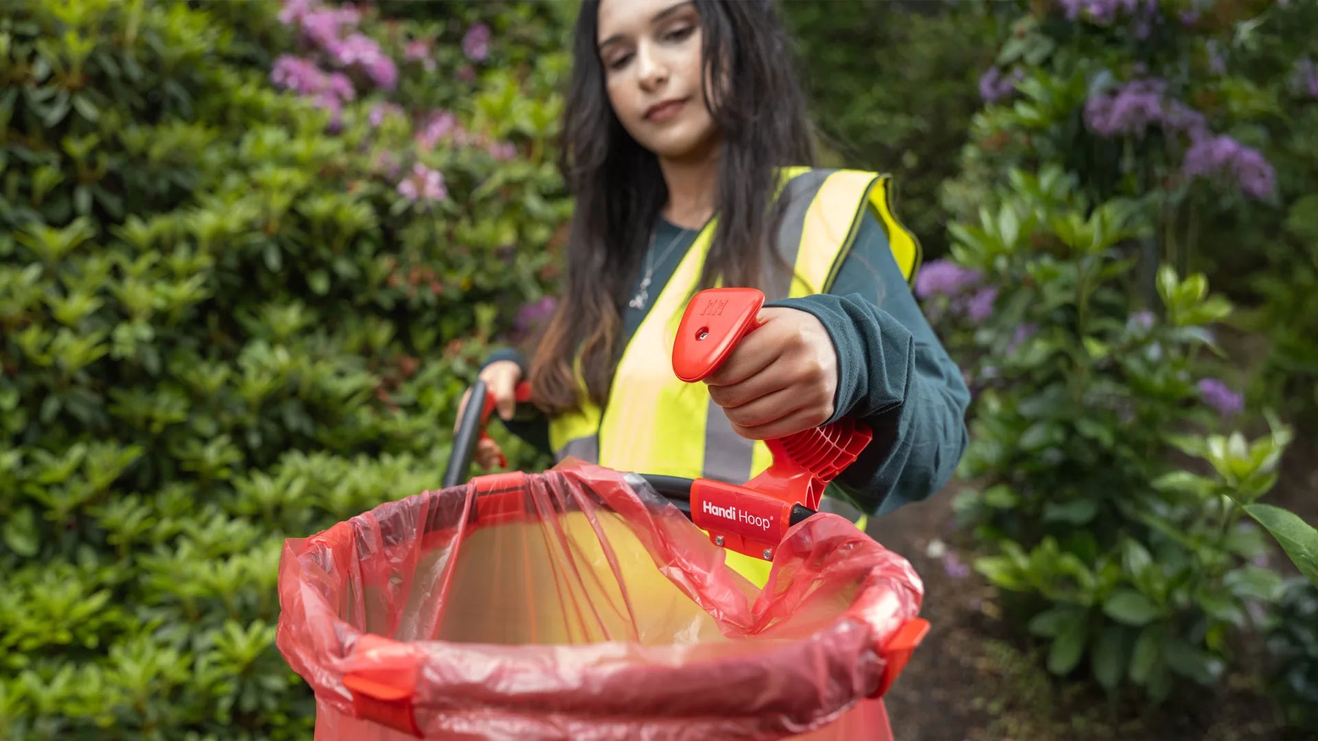 Person in a high-visibility vest holding Handi Hoop and litter picker in a garden setting.