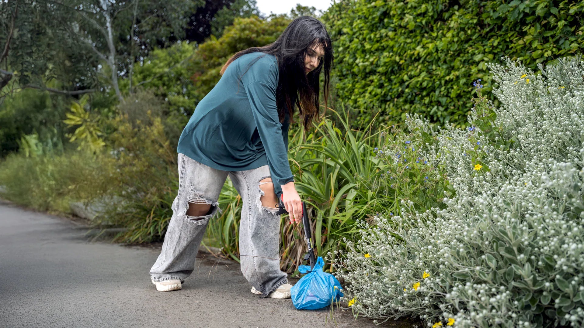 Person picking up animal waste on a path using the Handi Scoop pooper scooper.