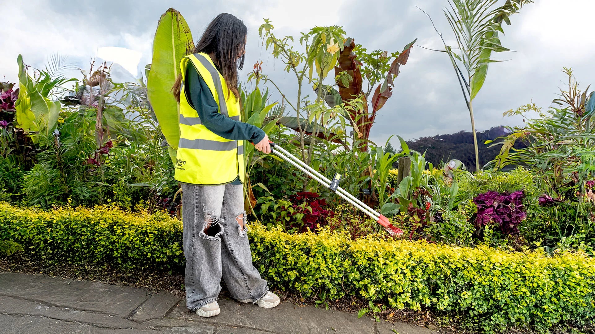 Person in a yellow safety vest using a Ranger Max to pick up litter from bushes.