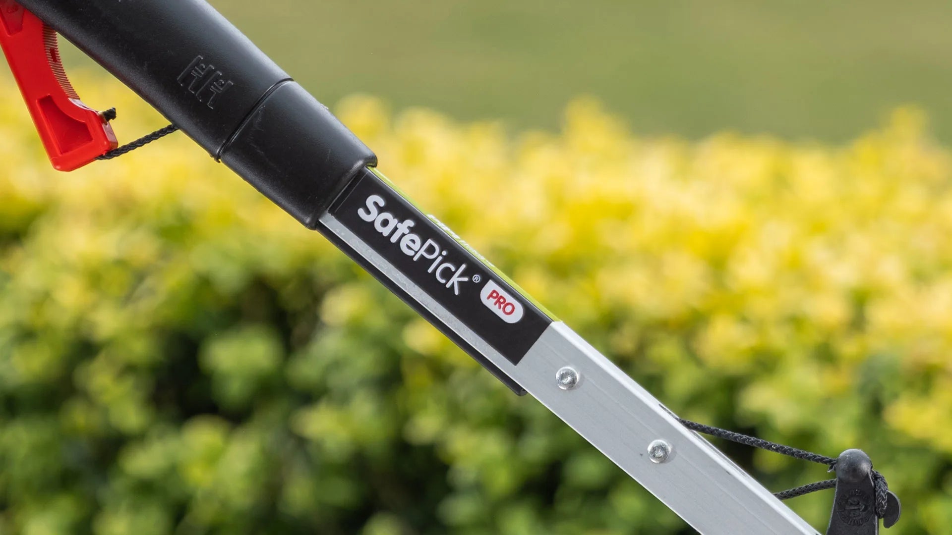 SafePick Pro litter picker held against blurred green and yellow garden.
