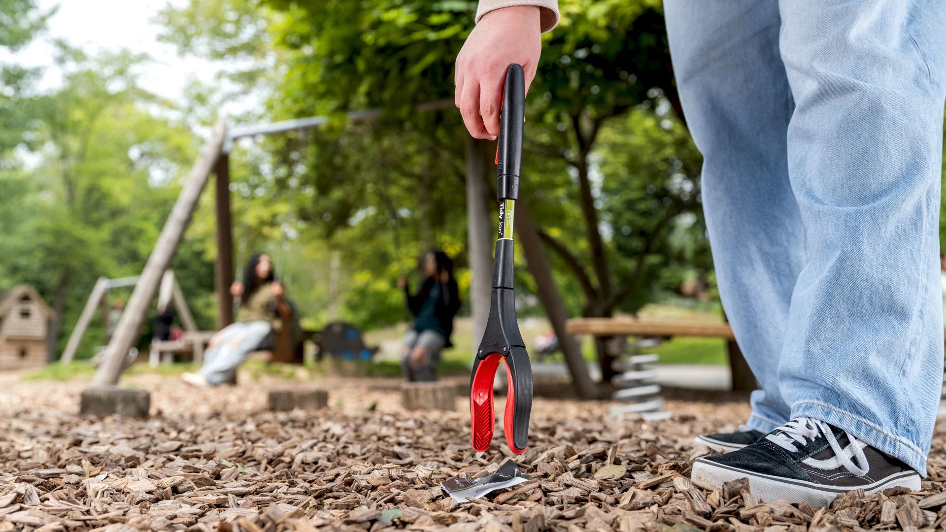 Person grabbing litter with the Tidy Jon litter picker on a playground.
