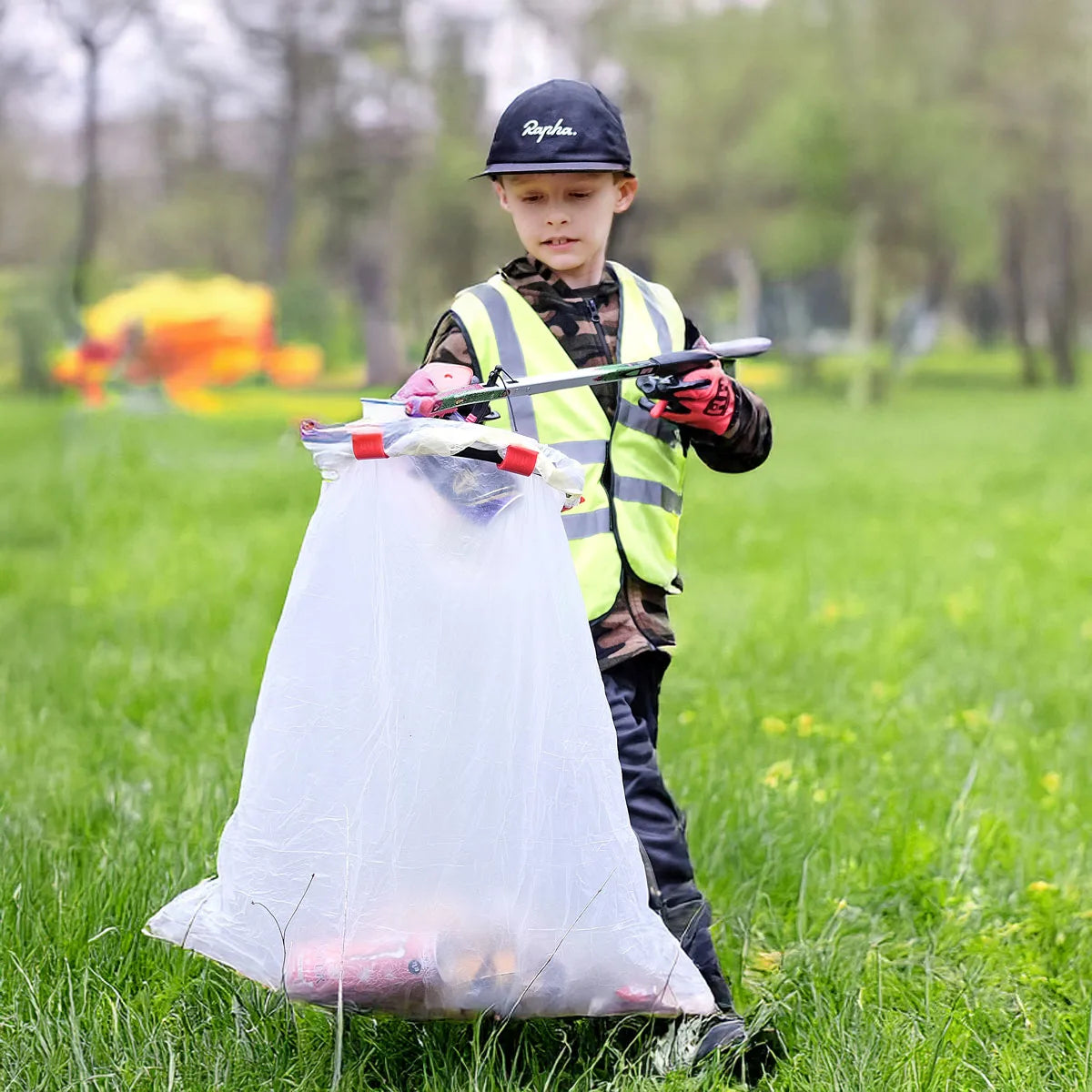 Child in a park with a Handi Hoop and litter picker, wearing a high-visibility vest and gloves.