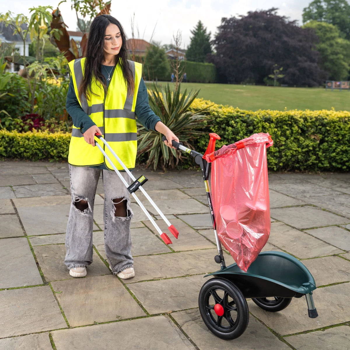 Volunteer in a yellow safety vest using Handi Cart Lite outside with grabber tool.