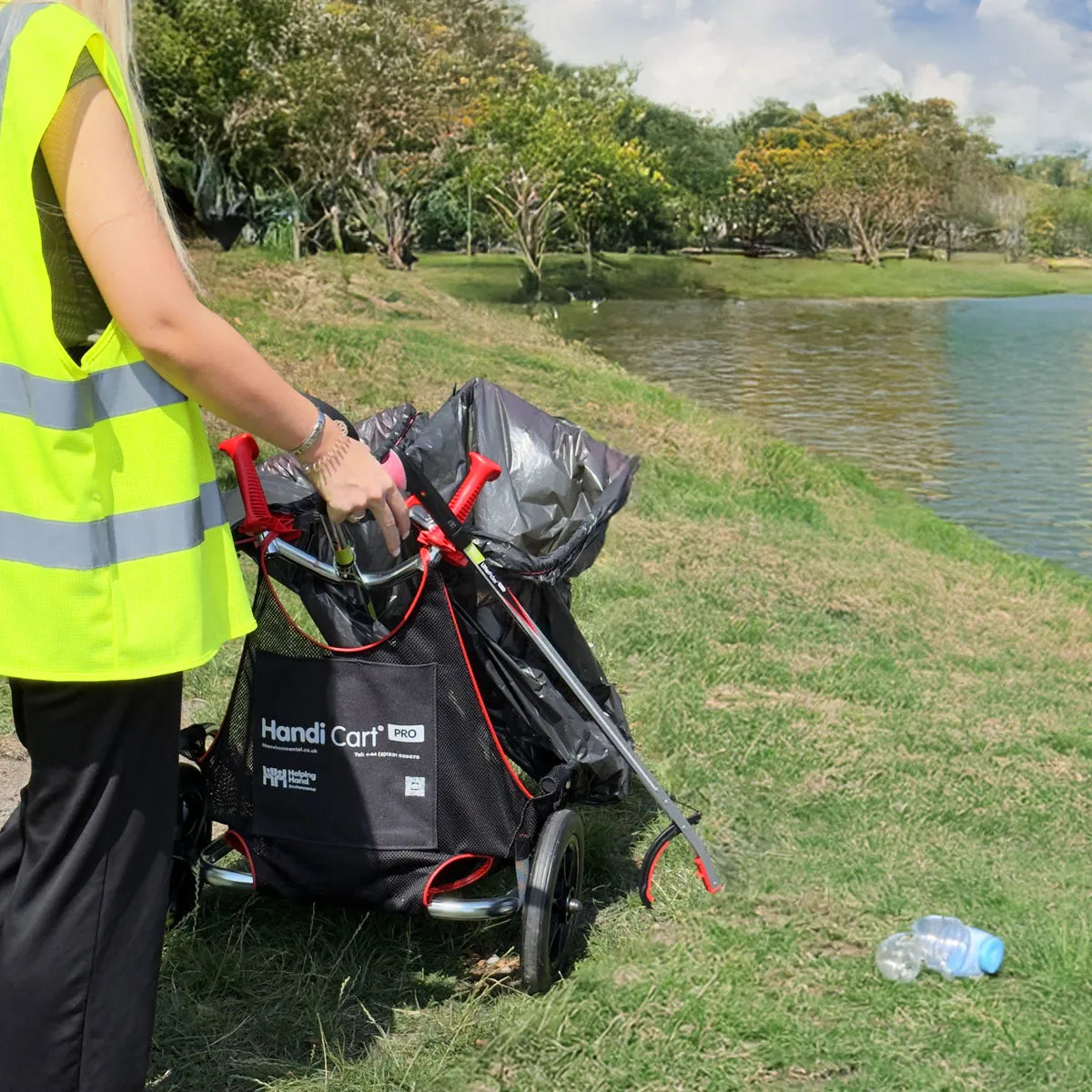 Volunteer in a yellow vest using Handi Cart Pro litter picking cart near lake.