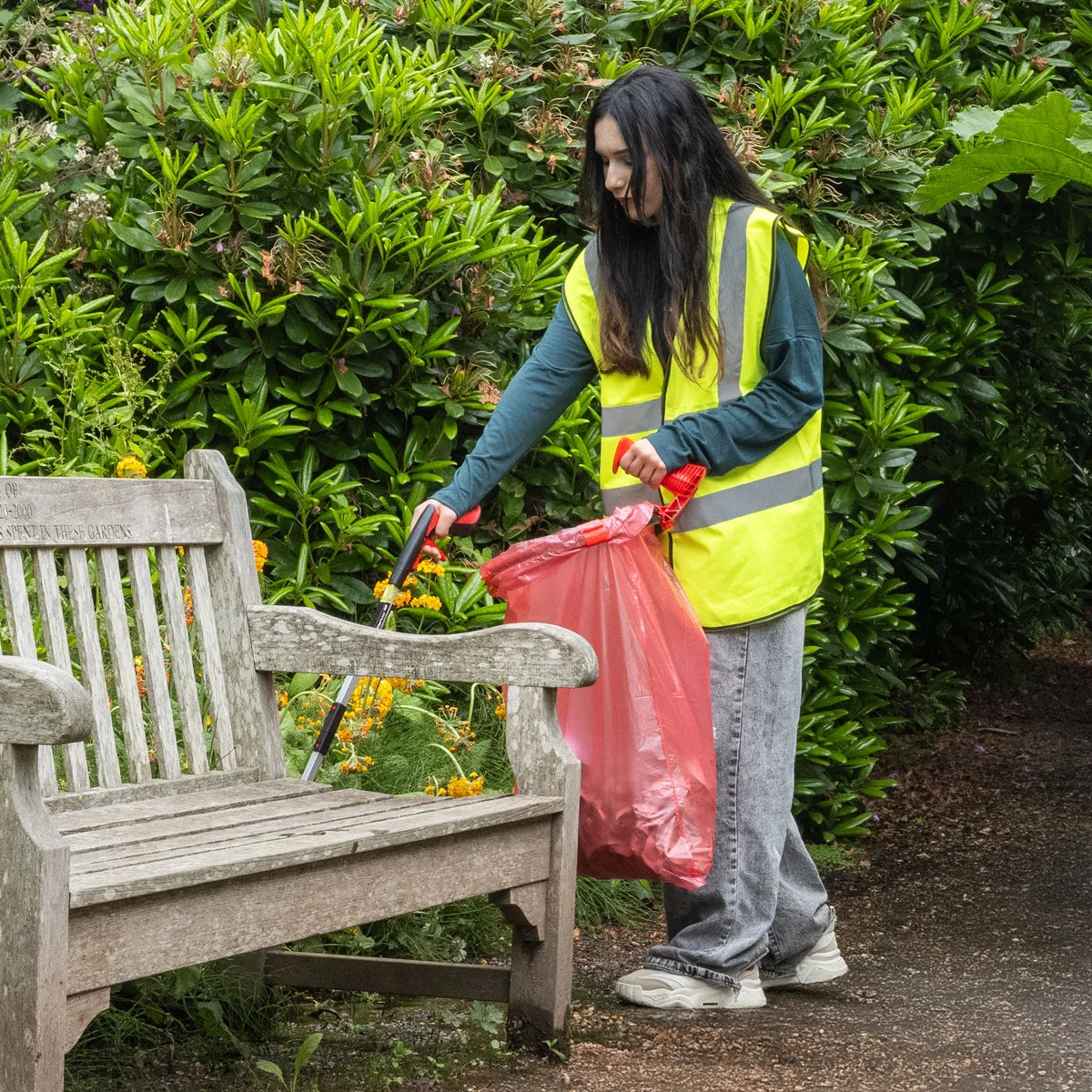 Person in a high-visibility vest cleaning up trash in a park setting with Handi Hoop Pro Clip litter hoop.