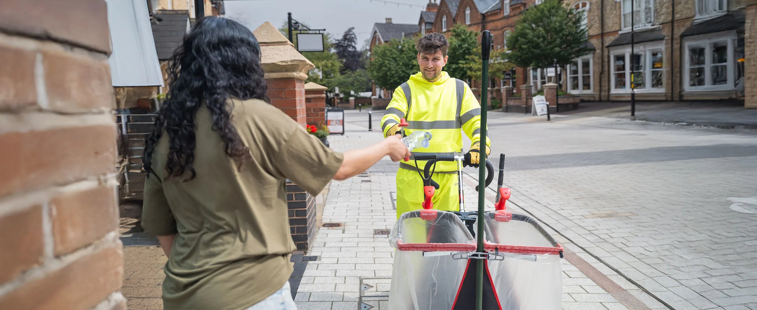 Person passing recyclable litter to a worker in high visibility clothing pushing litter cart.
