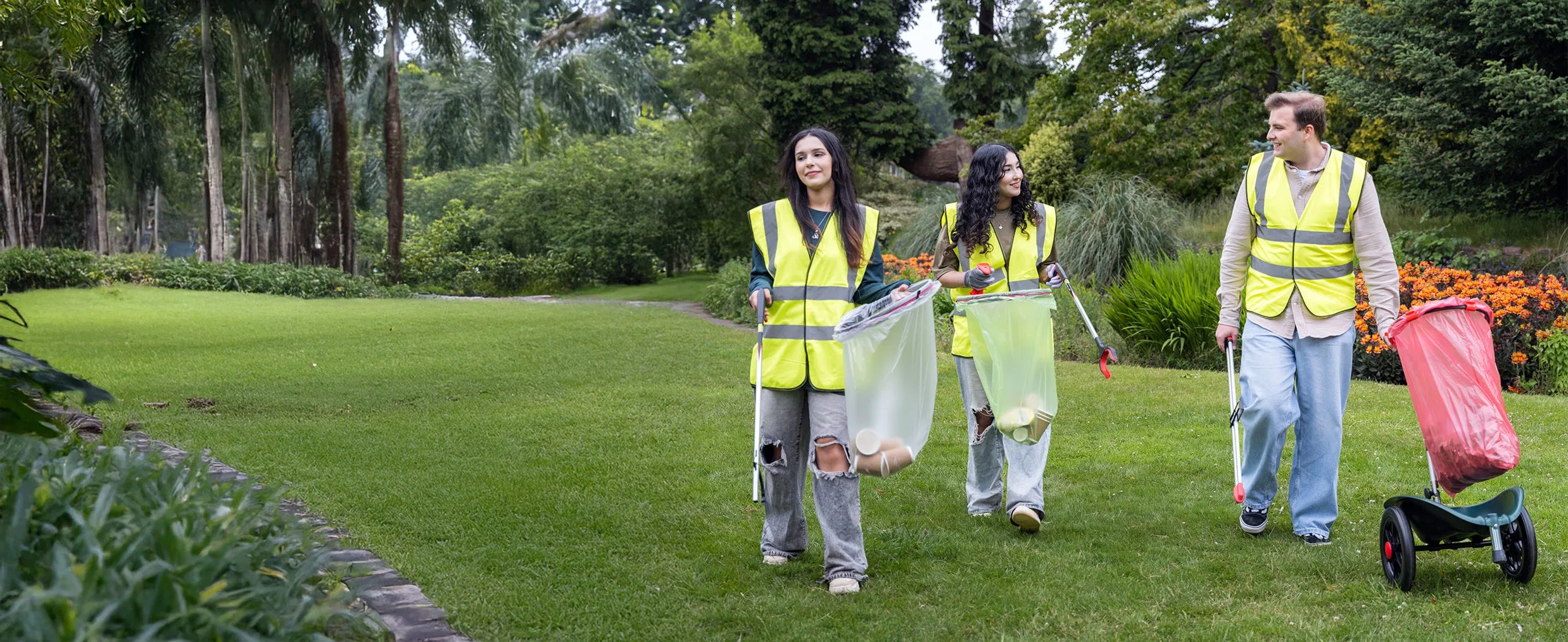 Three volunteers in high-visibility vests walking with Helping Hand litter picking carts and litter pickers