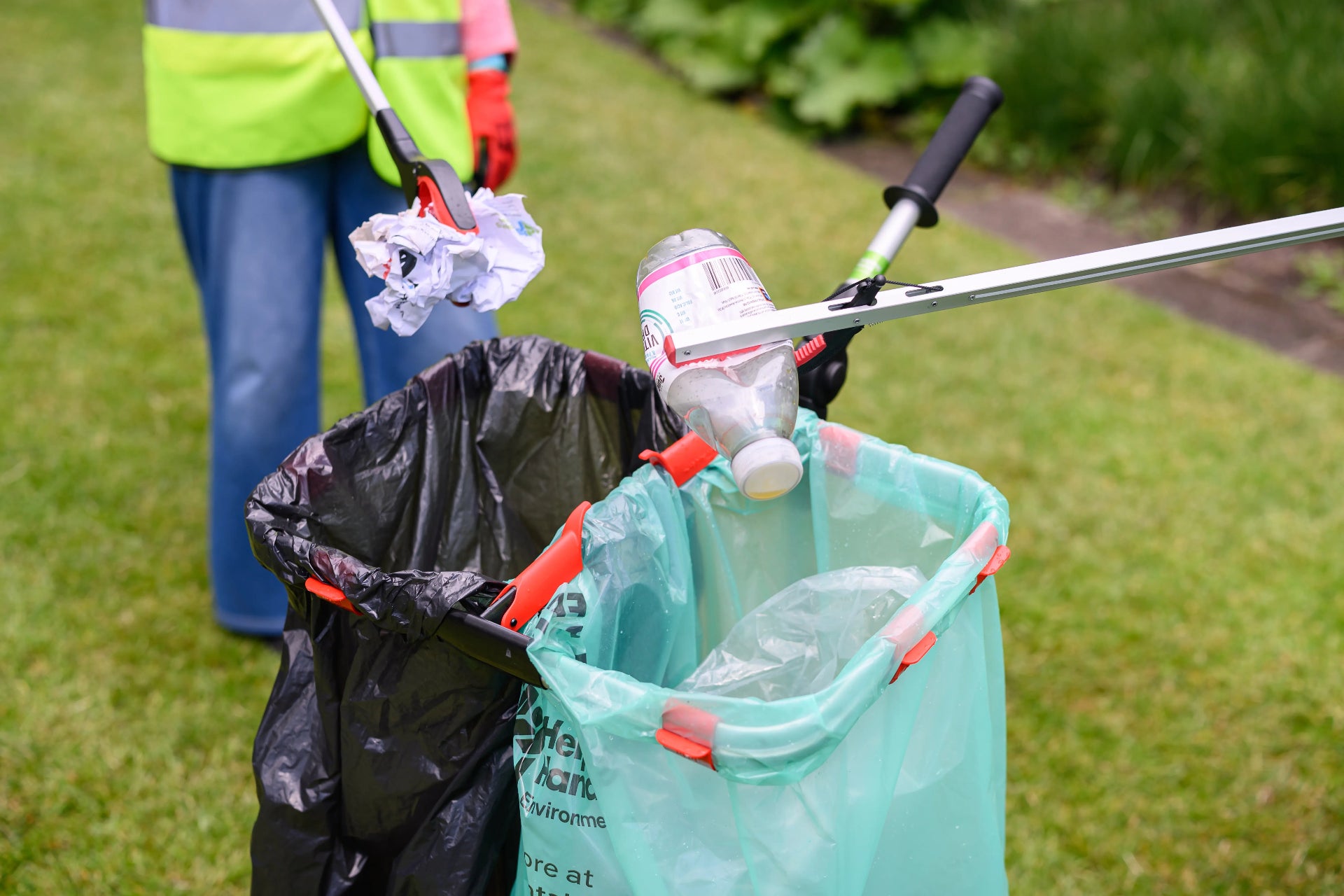 Person cleaning up trash with a litter picker on a grassy area