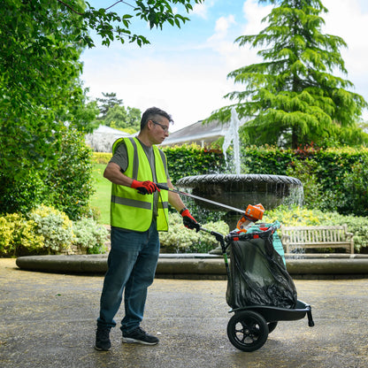 Person in a garden wearing a safety vest and pushing a litter cart.