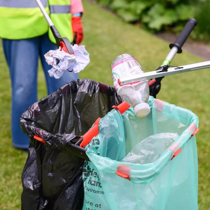 Person cleaning up trash with a litter picker on a grassy area