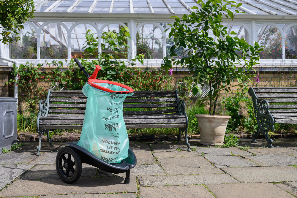 Green plastic bag with text on wheels in a garden setting