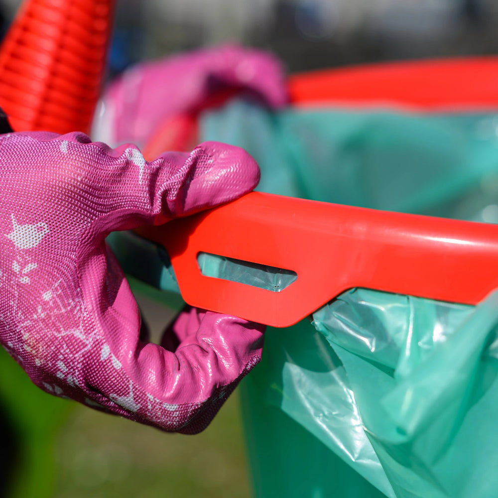 Person wearing pink gloves holding a red tool over a green trash bag.