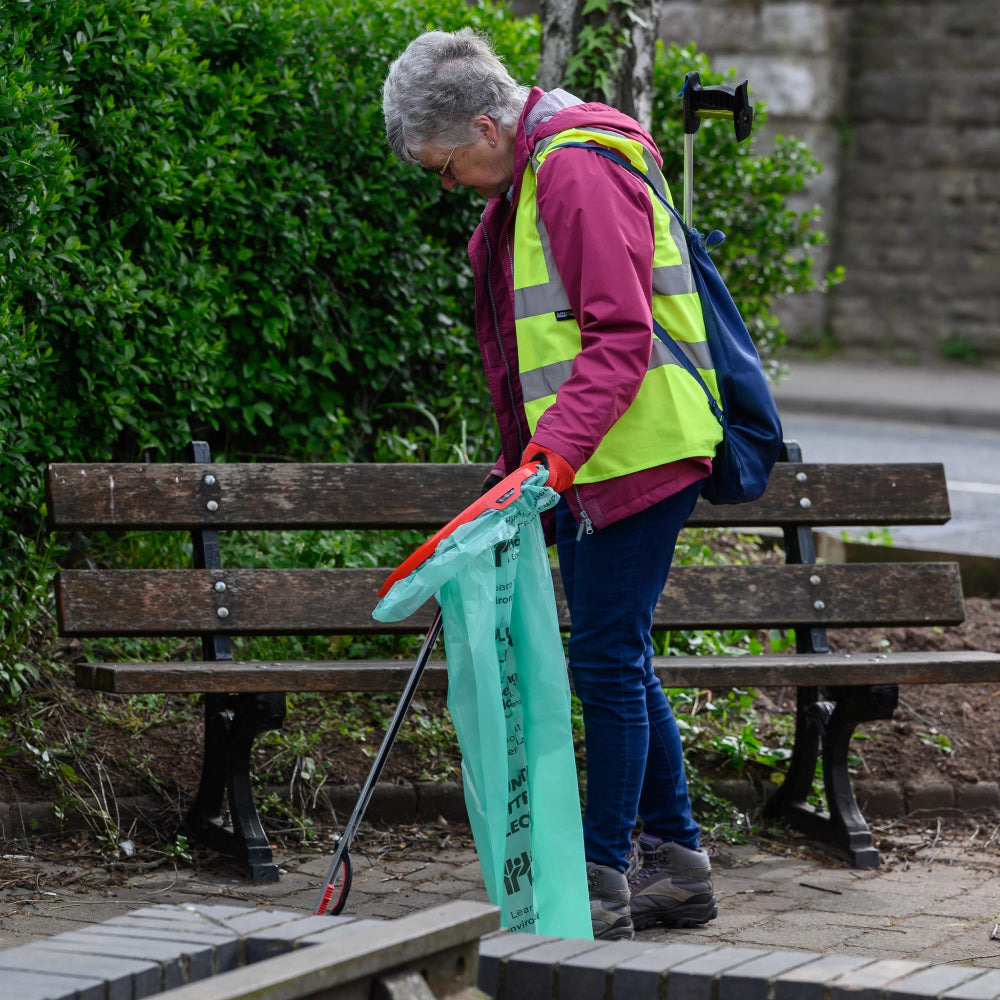 A picture of a person in a high vis vest using a litter picker and a litter hoop with a green bin bag
