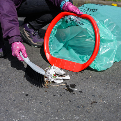 Person cleaning up litter on a road with a broom and trash bag.