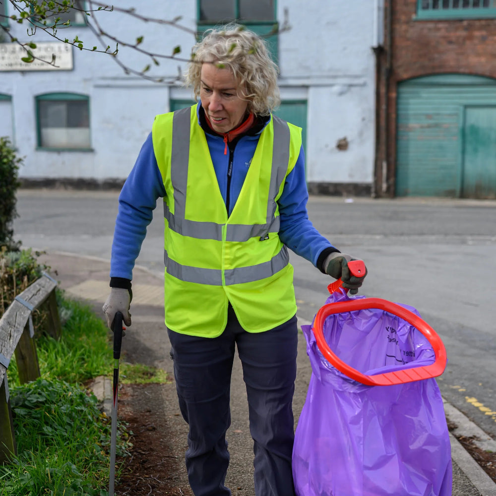 Person in high-visibility vest with purple bag and tool on a street