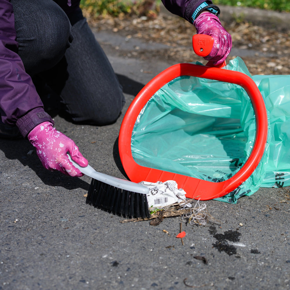 Person cleaning up trash with a broom and green bag on a street