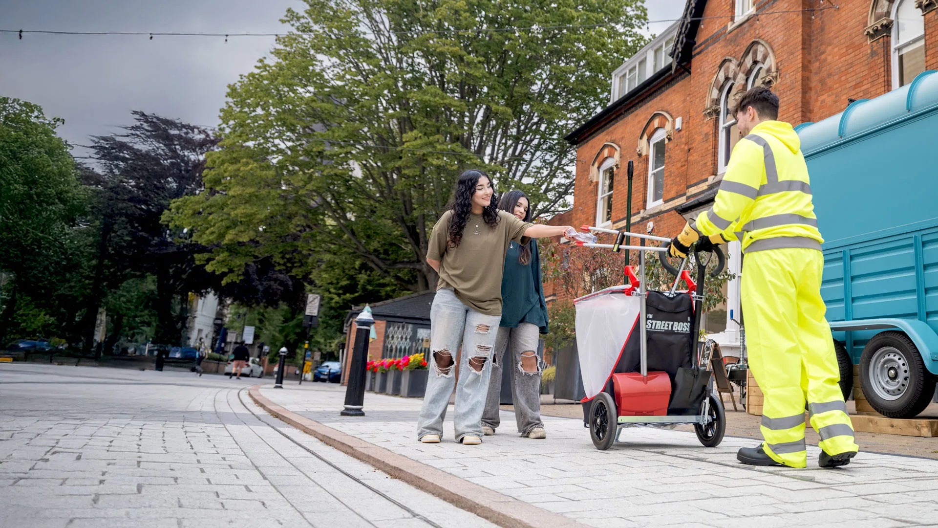 Person in high-visibility clothing grabbing litter from a woman using a litter picker.
