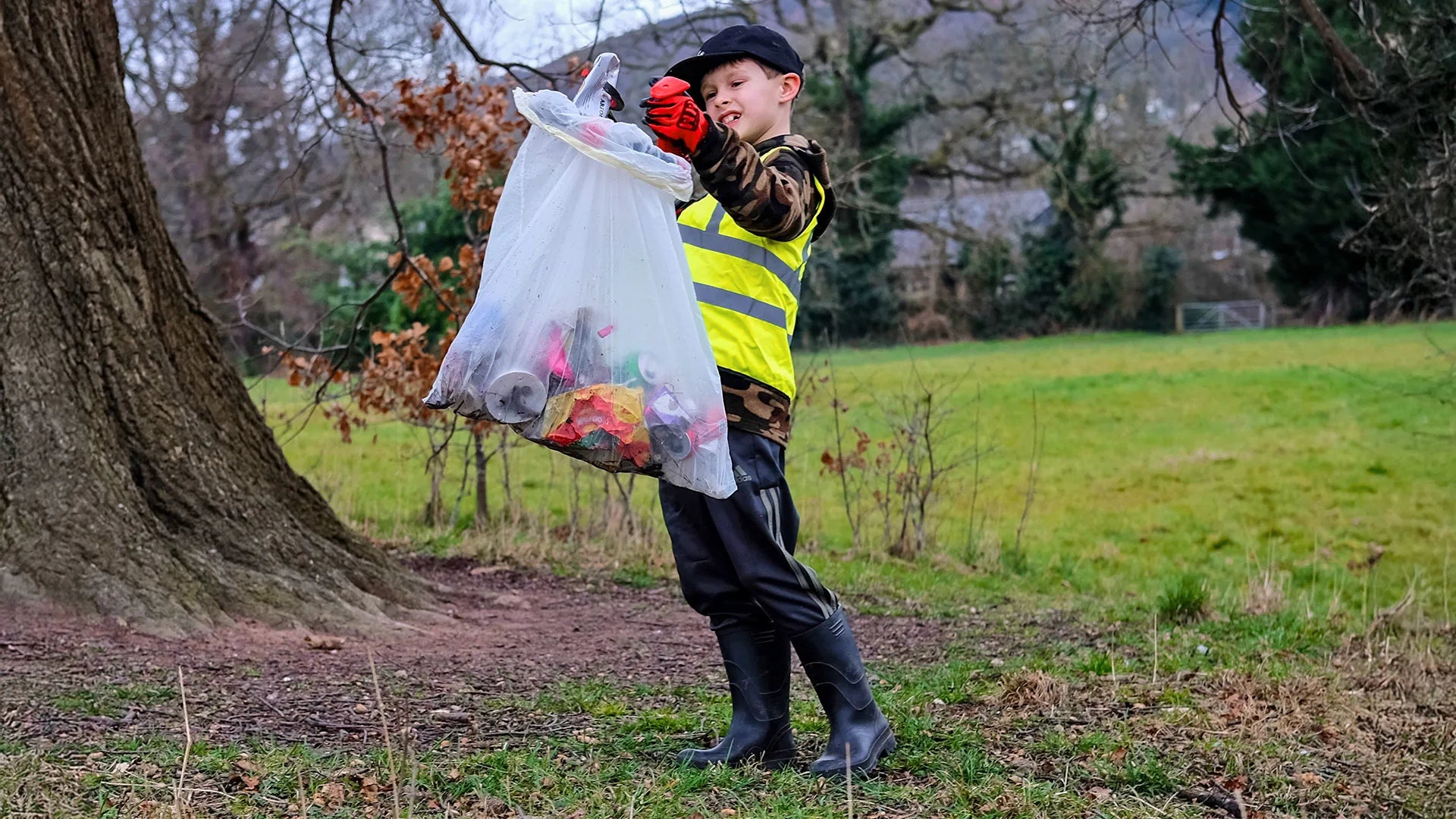 Child in a hi vis vest holding the Handi Hoop Kids filled with a bag of litter.
