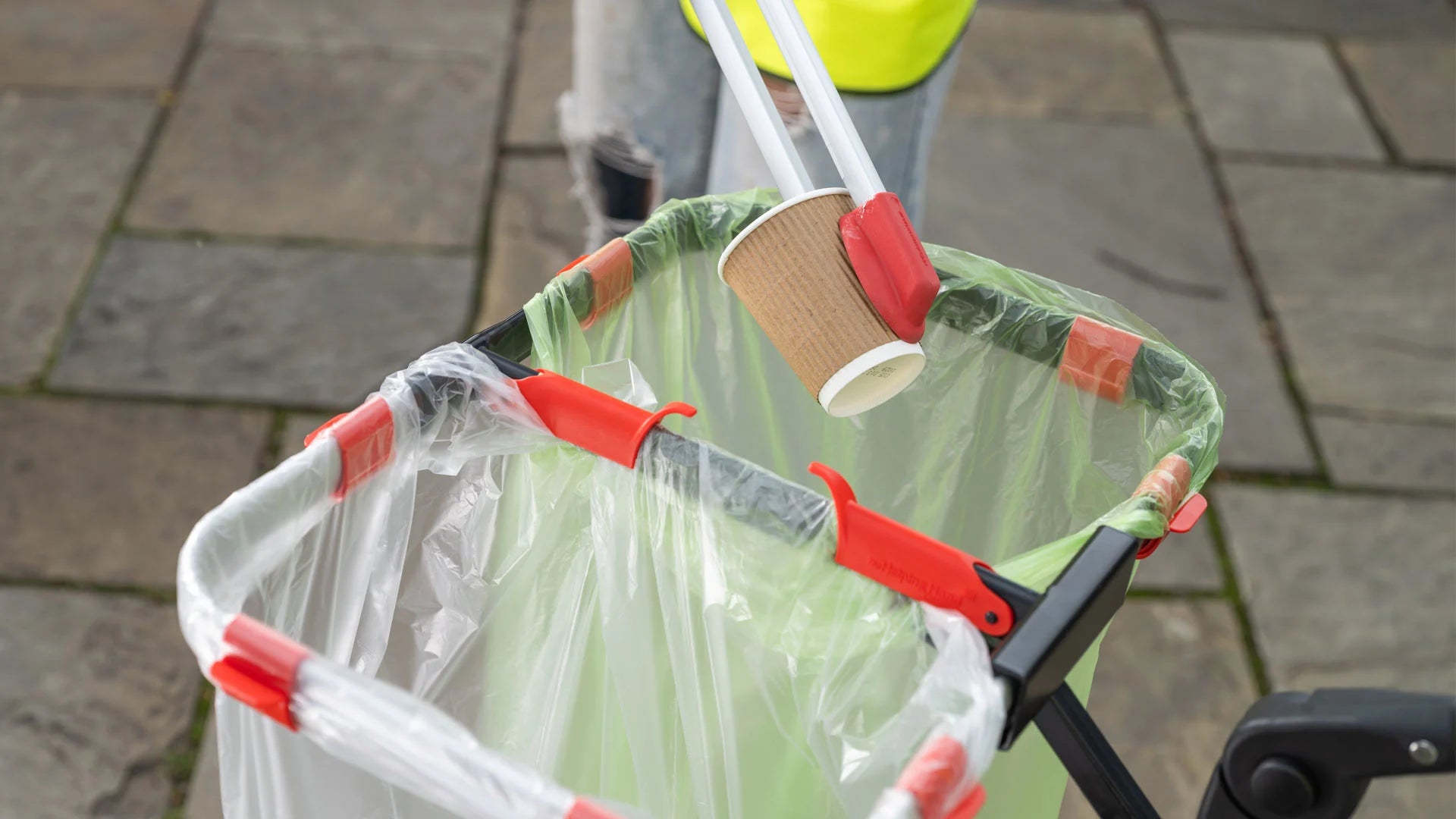Person using a litter picker to collect paper cup on a pavement.