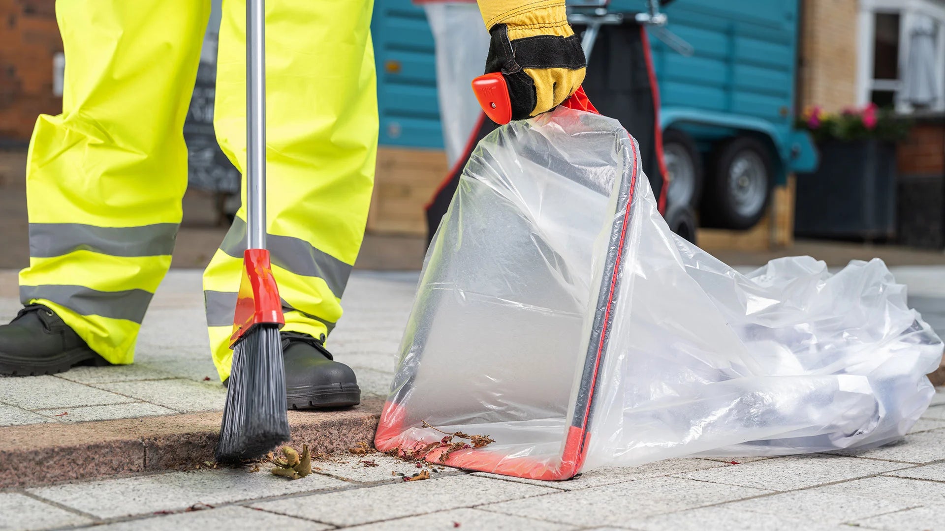 Person street cleaning a pavement with a broom and dustpan from the Street Boss cart.
