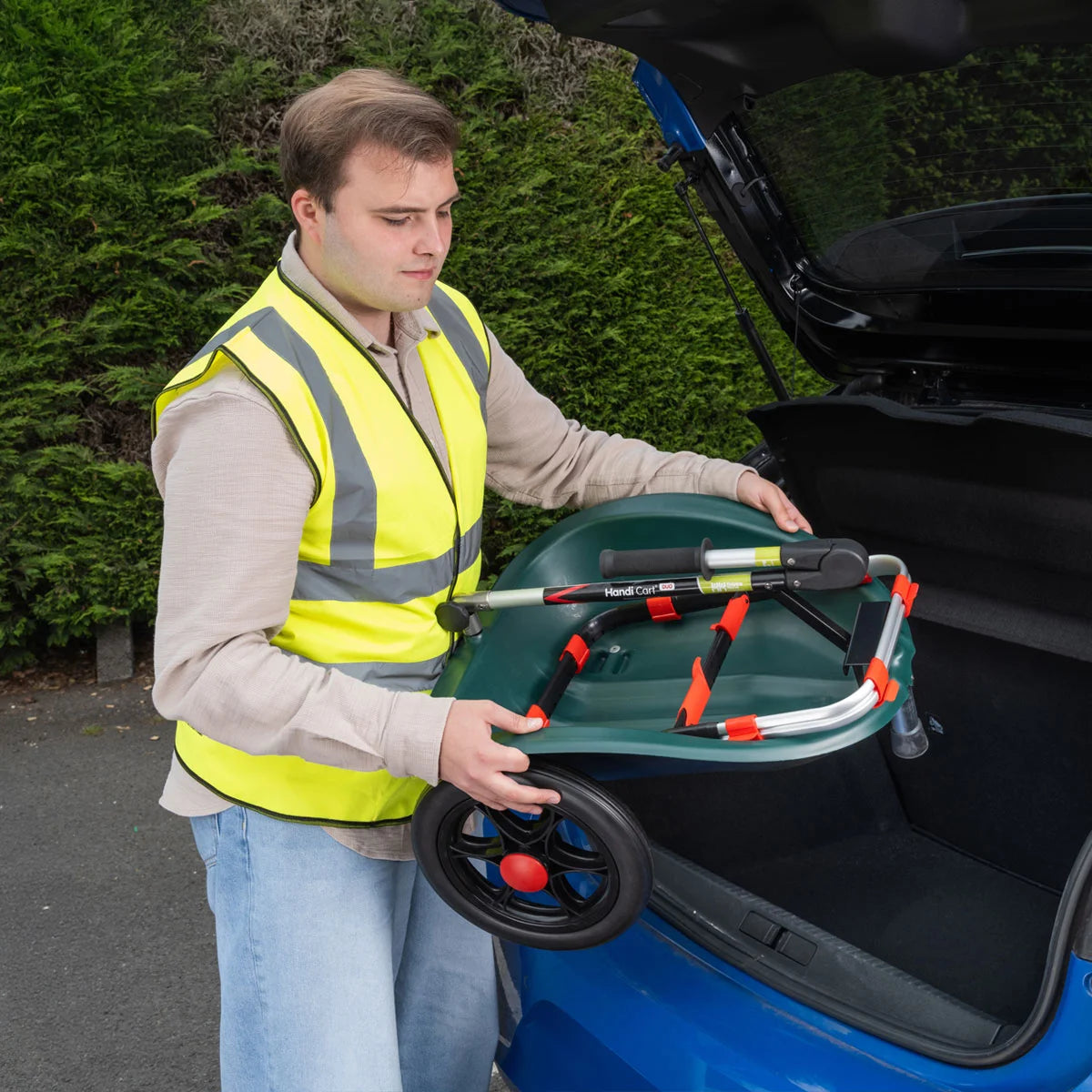 Man in a high-visibility vest putting Handi Cart Duo litter trolley open car trunk.