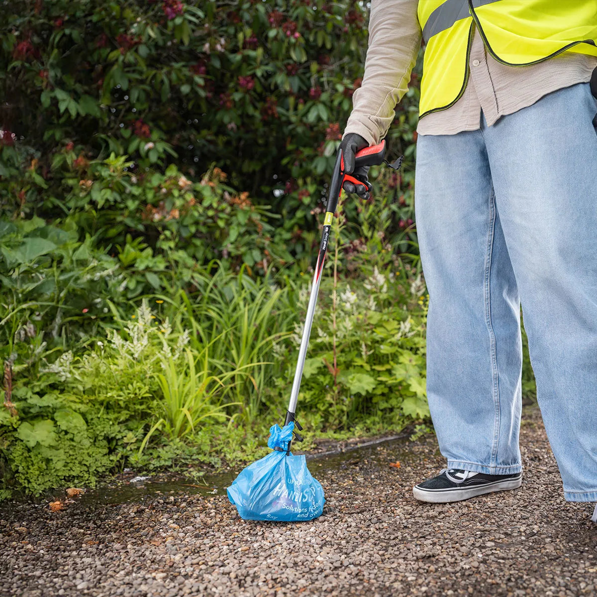 Person collecting animal waste on gravel with Handi Scoop Pro Poop Scoop.