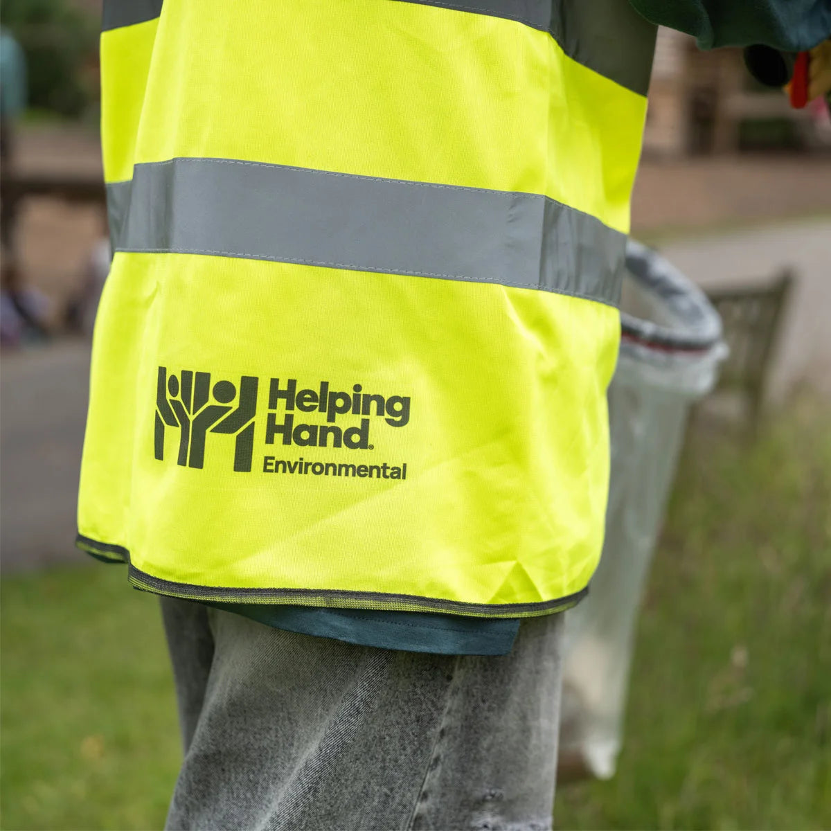 Person wearing a high-visibility jacket with 'Helping Hand Environmental' logo.