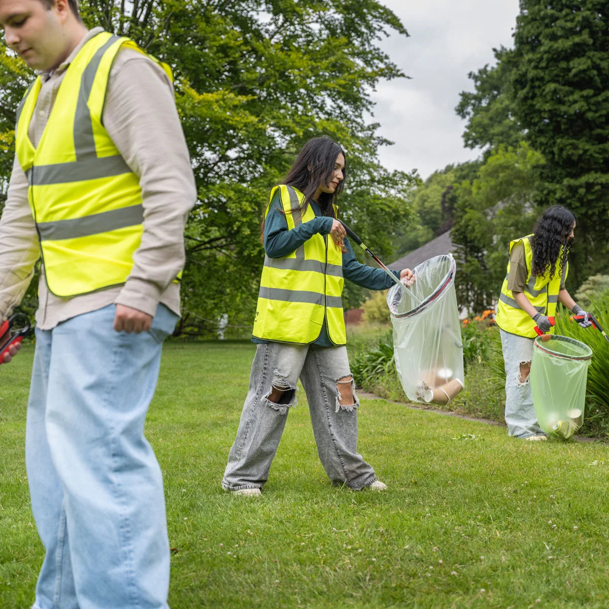 Volunteers in safety vests cleaning up a park with Helping Hand litter pickers 