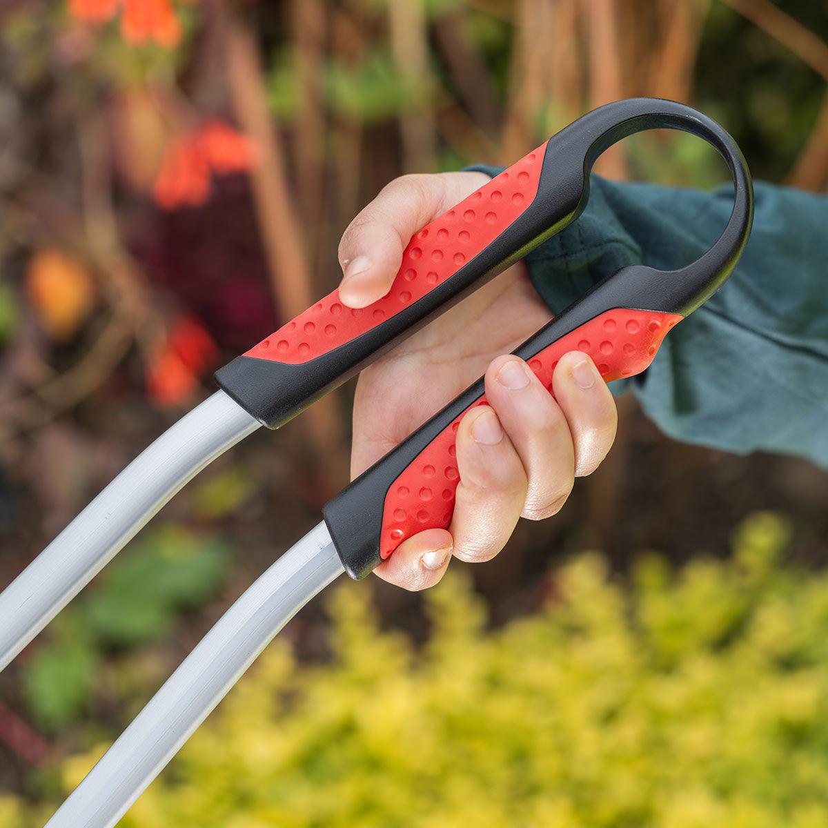 Hand holding a Ranger Max Curved heavy duty litter picker in a garden setting.
