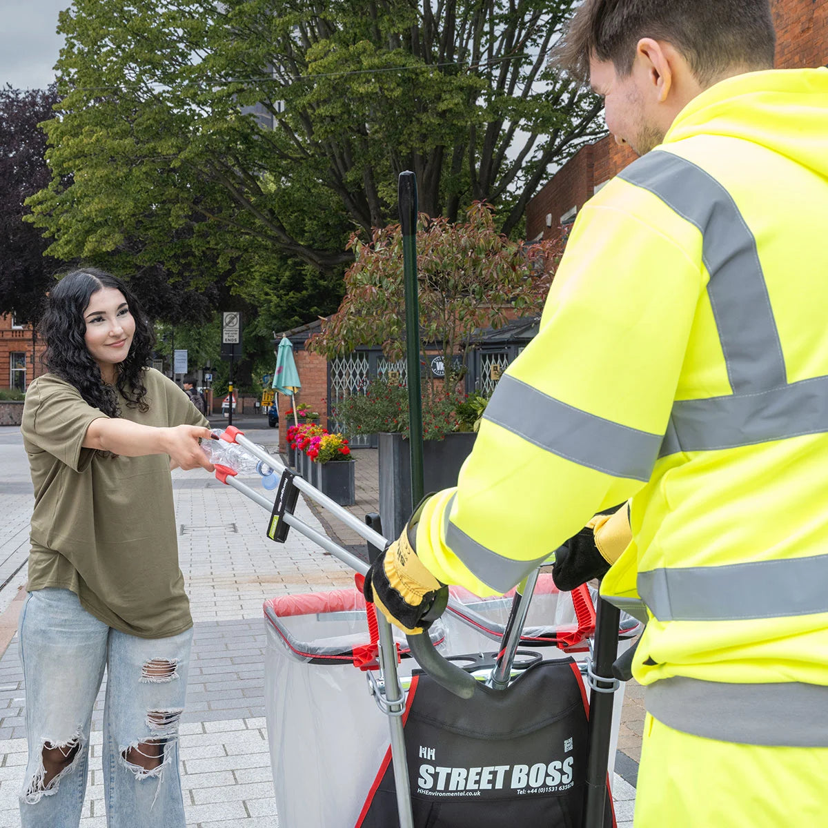Person in a high-visibility jacket interacting grabbing litter from a person with the Street Boss cart.
